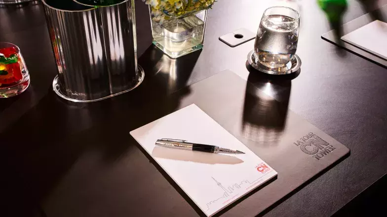 Vue détaillée d'une table de réunion avec un napperon portant la marque de la Tour CN, un bloc de papier et un stylo, un seau à glace individuel avec une boisson, un verre vide, un petit vase avec des fleurs, un verre rempli de bonbons, et un œillet de bureau pour la gestion des cordons.