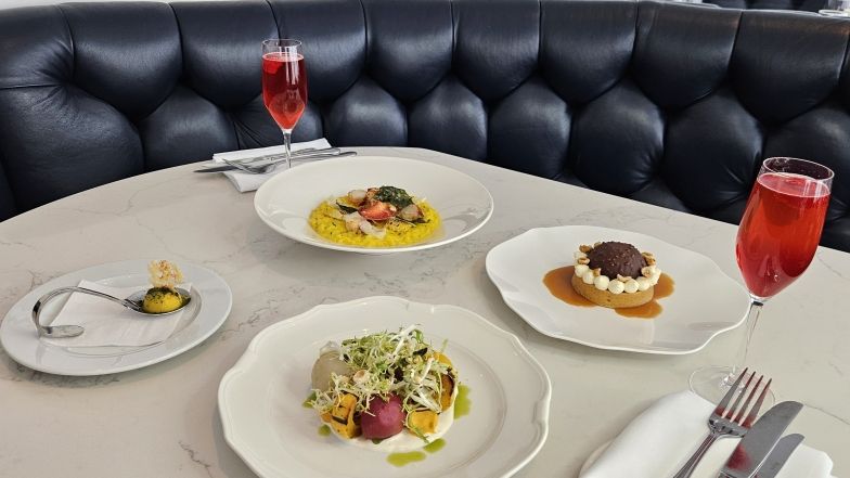 vue d'une banquette bleue et de 4 plats sur une table au restaurant 360. il y a aussi deux flûtes à champagne remplies d'un cocktail rouge.