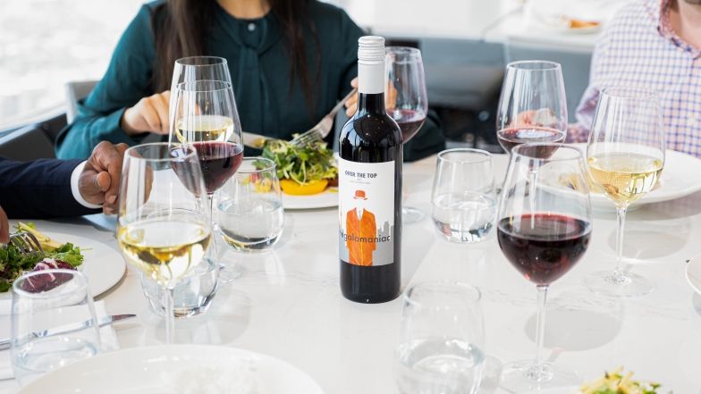 Groupe assis à une table au 360. La table est ronde et en marbre blanc, remplie de verres à vin et d'assiettes. Une bouteille de vin rouge 360 se trouve au centre de la table.