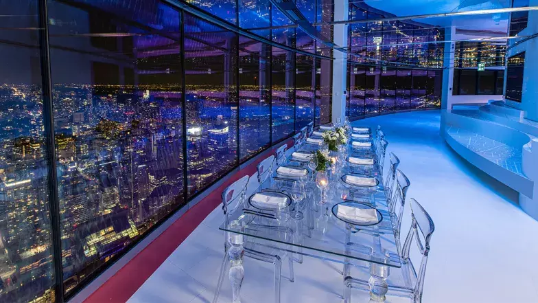 Chaises et table installées le long de la fenêtre avec vue sur Toronto la nuit.