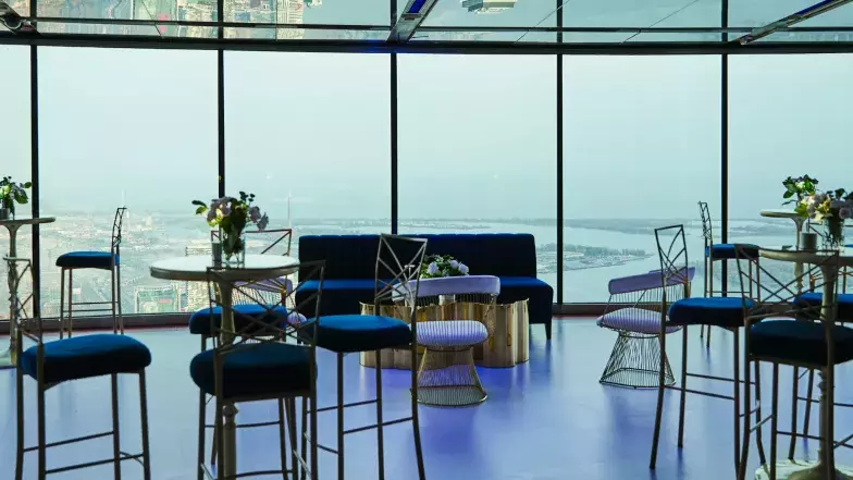 Configuration d'un événement privé au niveau d'observation principal de la Tour CN avec des tables hautes, des canapés, des lampes et des fleurs. En arrière-plan, on aperçoit la vue de Toronto et du lac Ontario à travers les fenêtres.