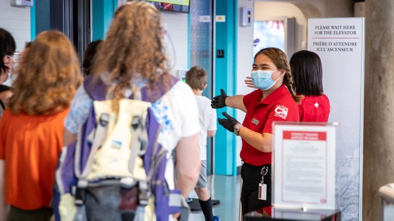 Un employé de la Tour CN portant un masque et une paire de gants salue les gens qui attendent les ascenseurs.