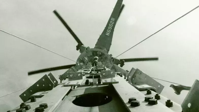 Une ancienne photo montrant un hélicoptère au-dessus de la tour. Une personne se trouve au sommet de la tour.