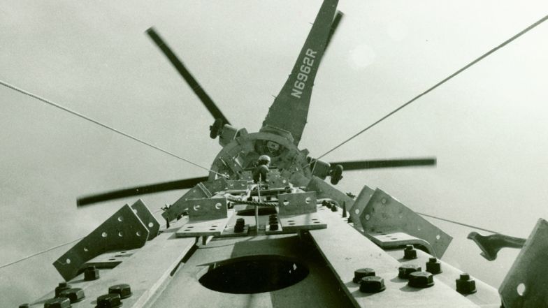 Une ancienne photo montrant un hélicoptère au-dessus de la tour. Une personne se trouve au sommet de la tour.