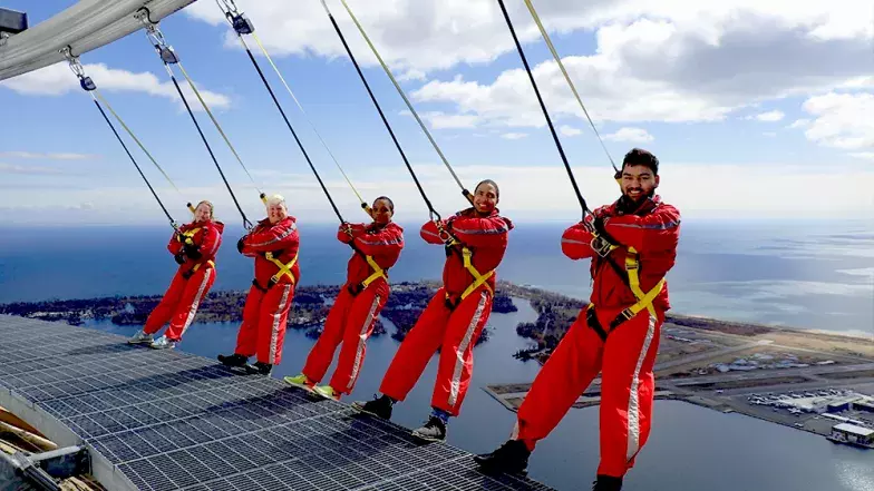 Groupe de cinq personnes penché en arrière sur le bord. Nuages et ciel bleu derrière eux.