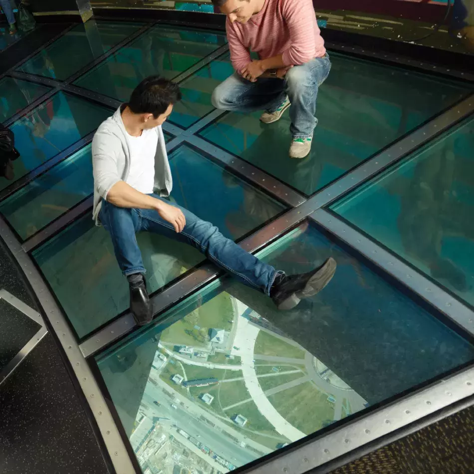 Deux personnes assises sur le sol en verre. Le sol est visible loin en dessous.