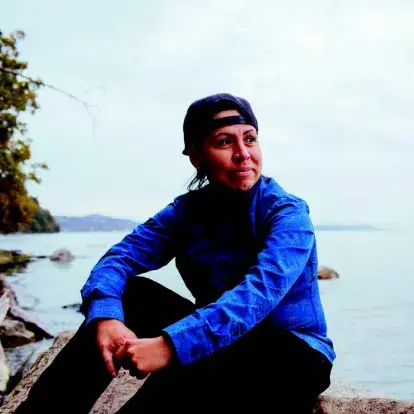 Female artist Margaret August seated, with a serene body of water in the background.