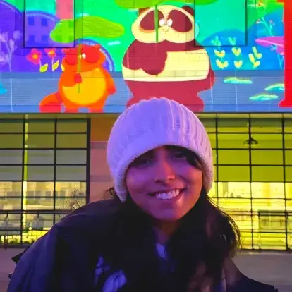 Portrait de Fatimah I à l’extérieur de nuit, portant un bonnet et une veste, avec une murale colorée en arrière-plan.
