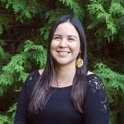 Portrait de l'artiste mohawk et cree Katie Longboat debout et souriante devant des arbres