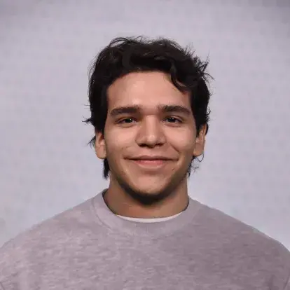 Portrait de Saul Benavides faisant face à la caméra sur un fond studio uni, avec des cheveux courts foncés et un haut de couleur neutre