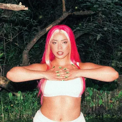 Portrait de Semiah Smith, debout à l'extérieur, vêtue d'une tenue blanche et arborant une chevelure d'un magenta éclatant.