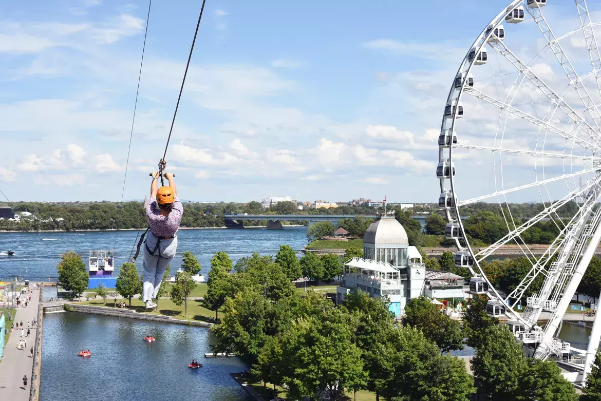 Une personne qui descend une tyrolienne près de la grande roue du Vieux-Port de Montréal.