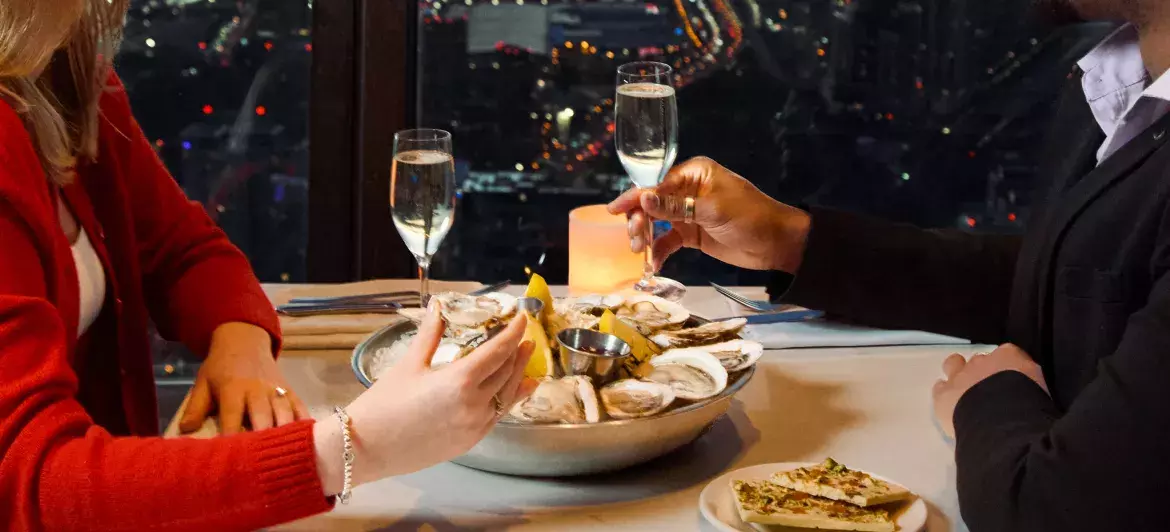 Un couple déguste des huîtres fraîches, du chocolat et du champagne au restaurant 360. En arrière-plan, on peut voir la vue de Toronto la nuit à travers les fenêtres.
