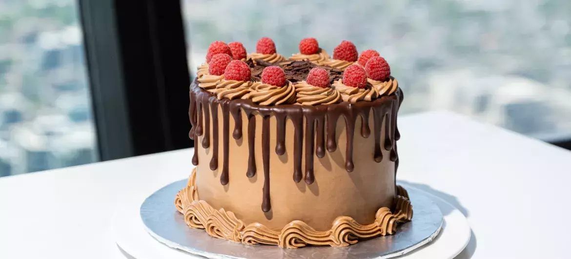 Vue d'un gros gâteau au chocolat décoré de framboises posé sur une table en marbre blanc au restaurant 360. En arrière-plan, on peut voir la vue de Toronto à travers les fenêtres.