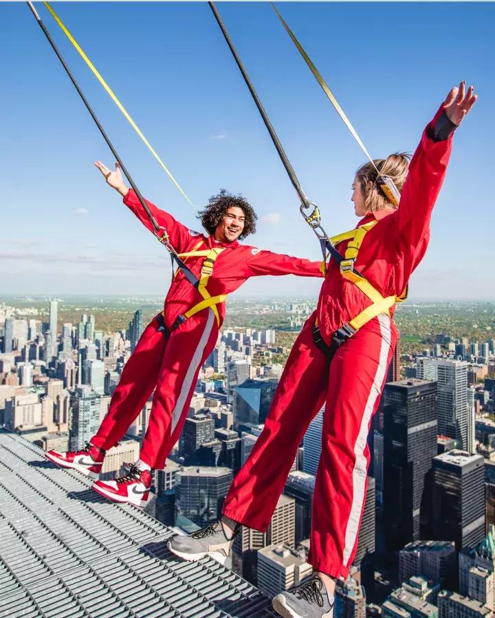 Deux personnes se penchant vers l'arrière par-dessus le bord, avec la ville de Toronto en contrebas.